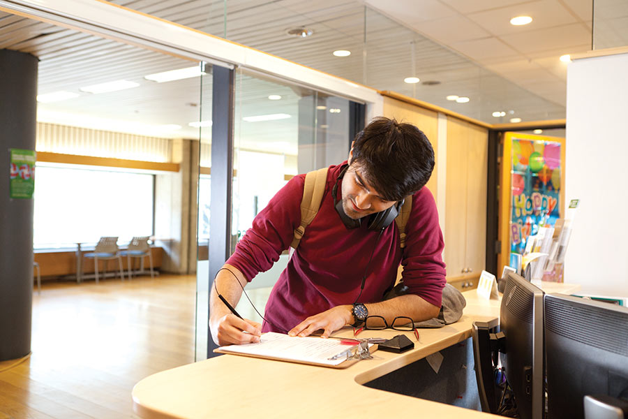 Student at the front desk of the Office of Residence and Student Life applying for a music pass.
